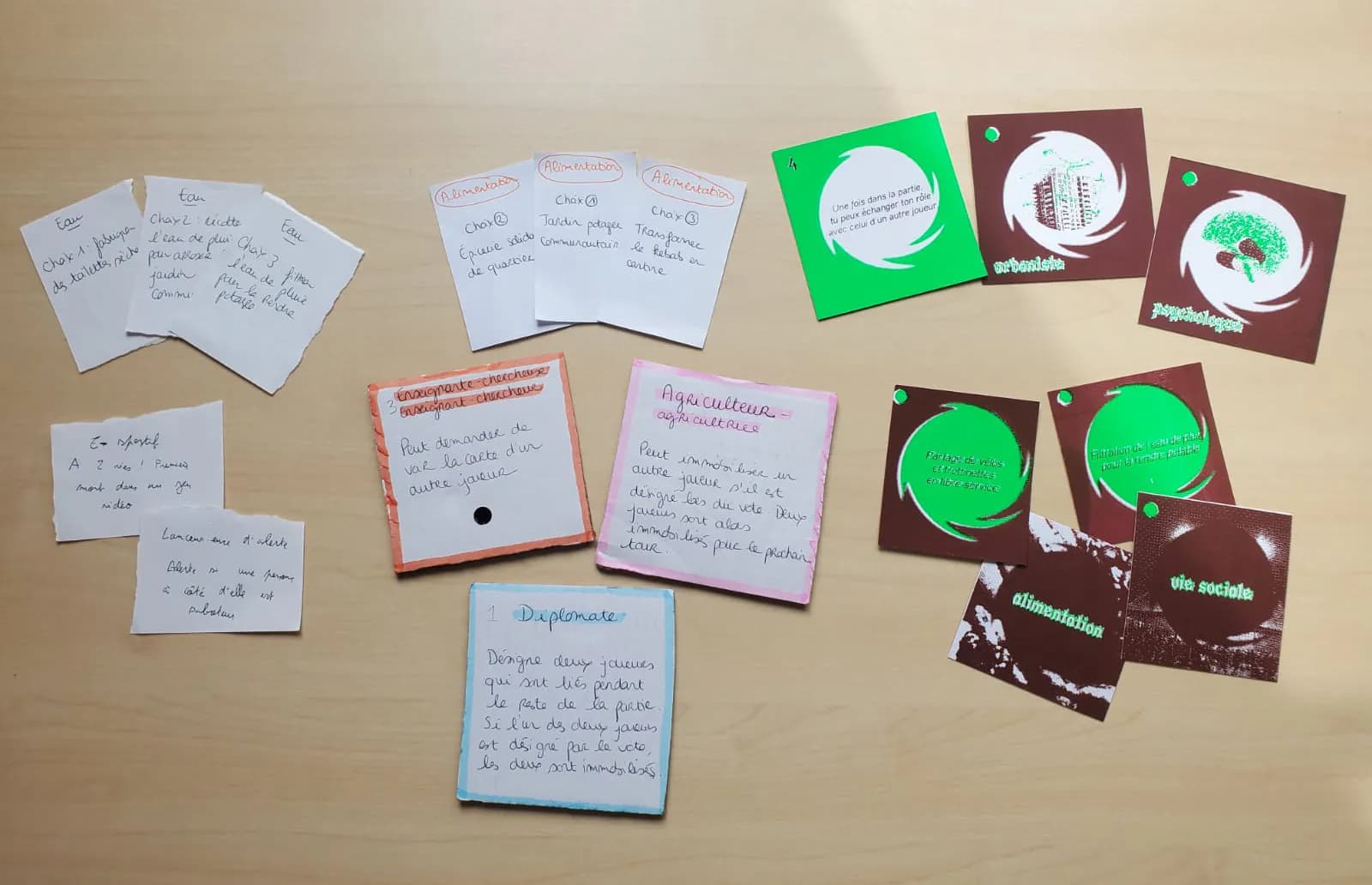 Prototypes du jeu sur une table : cartes manuscrites et cartes imprimées bordeaux et vertes