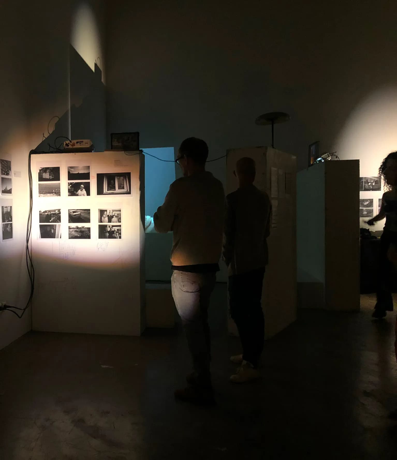 Vue de l’installation : des visiteurs dans une salle sombre, devant des cimaises de photographies noir et blanc