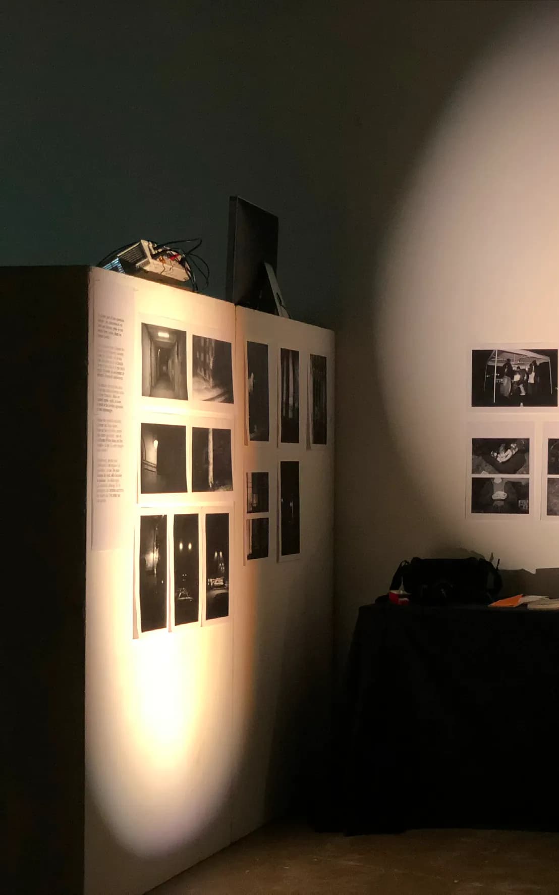 Vue de l’installation : une cimaise éclairée par un faisceau, photographies noir et blanc et texte