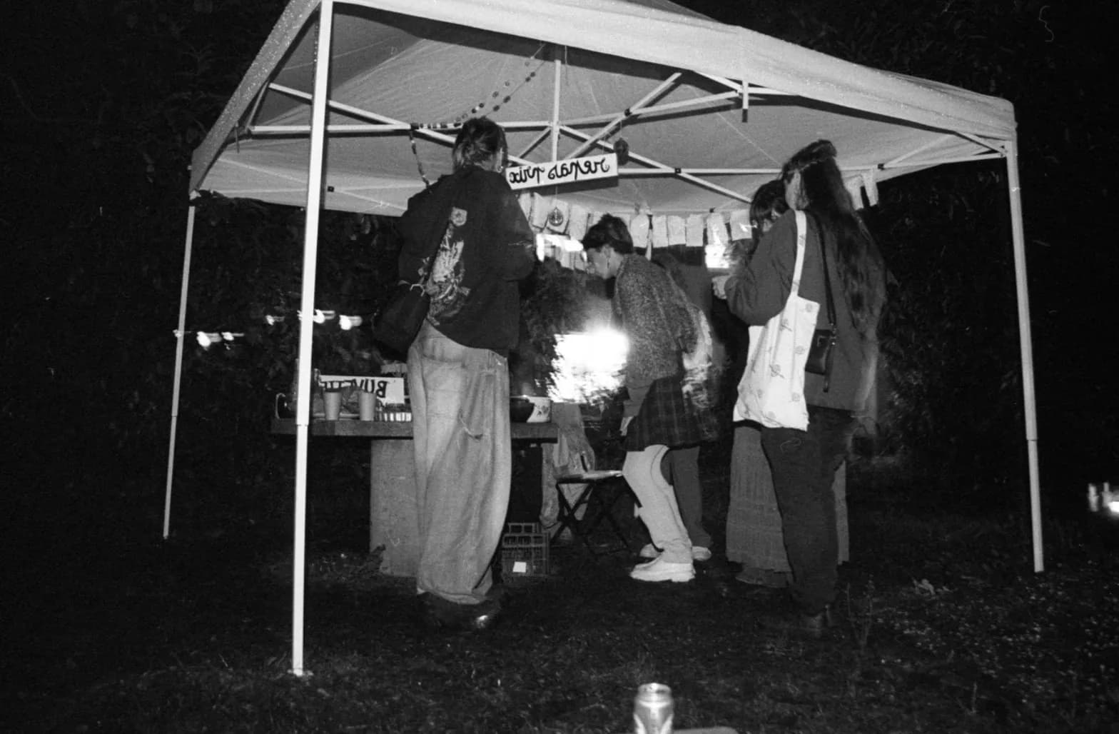 At night, people gathered under a lit gazebo, black and white